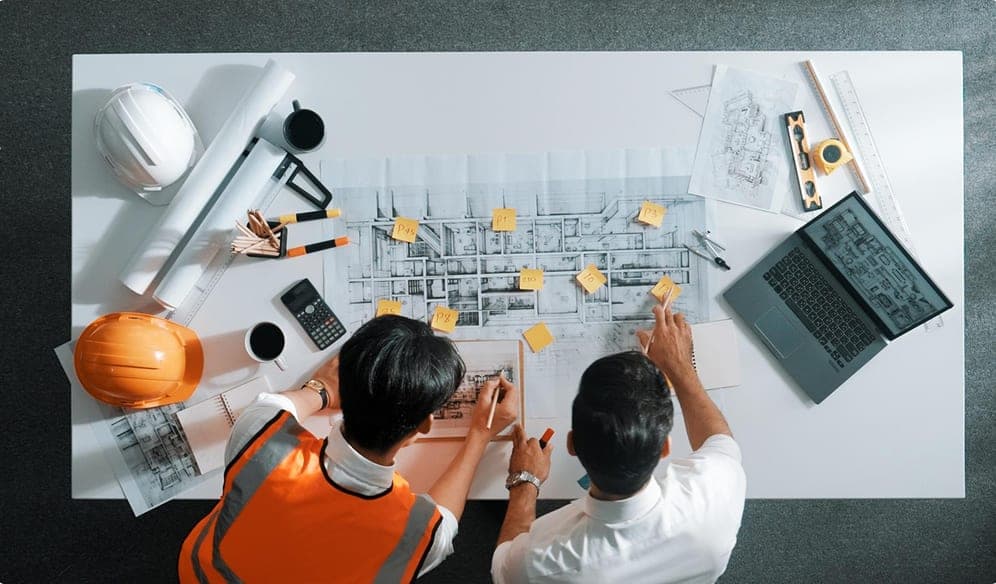 Workers discussing equipment over spread-out drawings