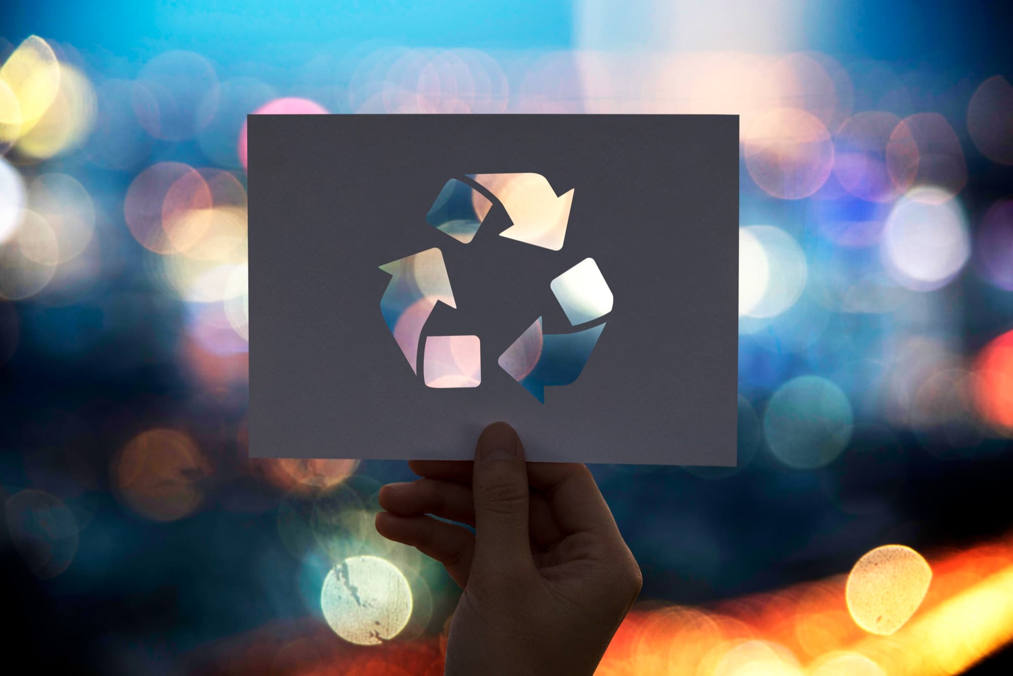 A hand holding up a card cut with the recycling symbol